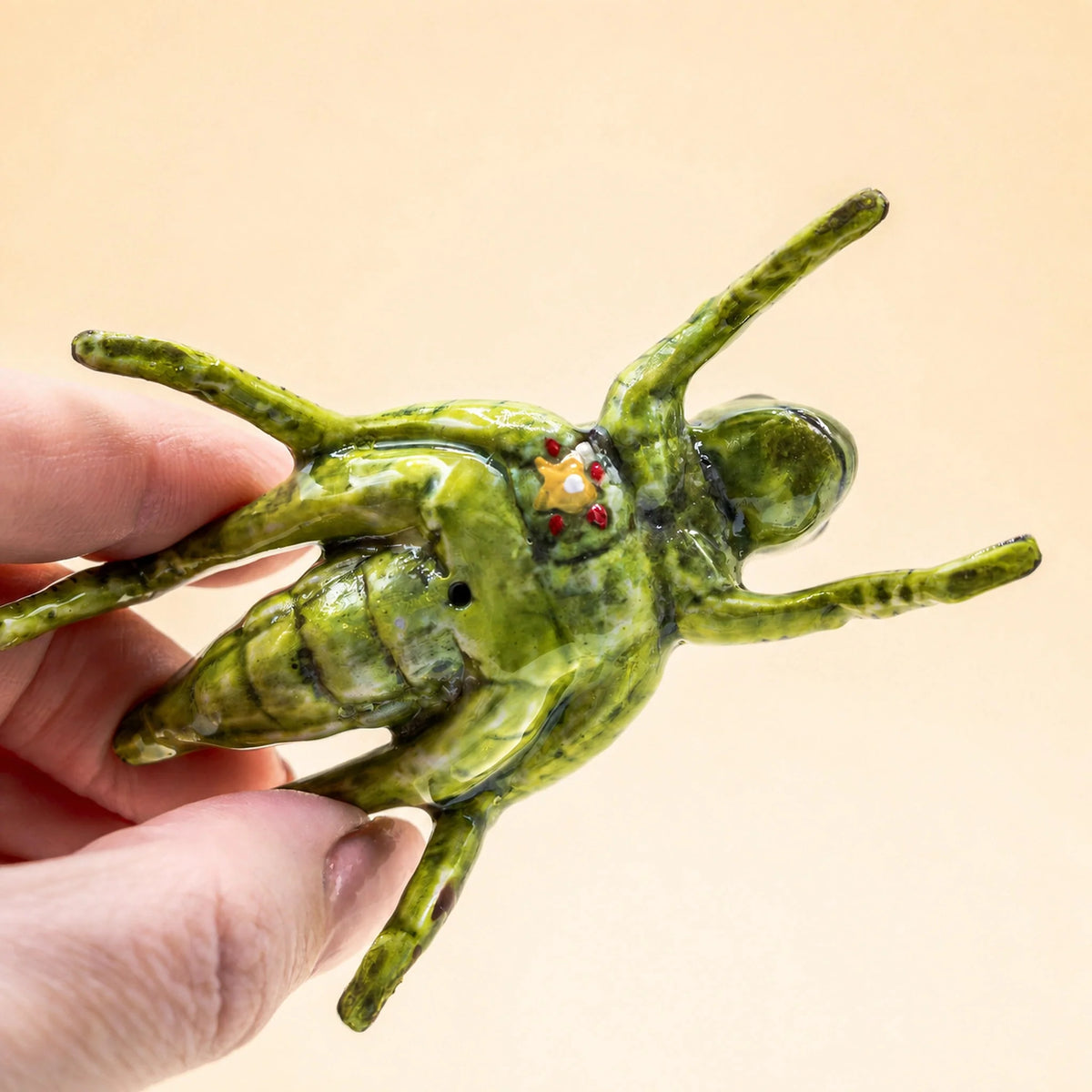 Hand holding the Camp Hollow porcelain cricket cake topper