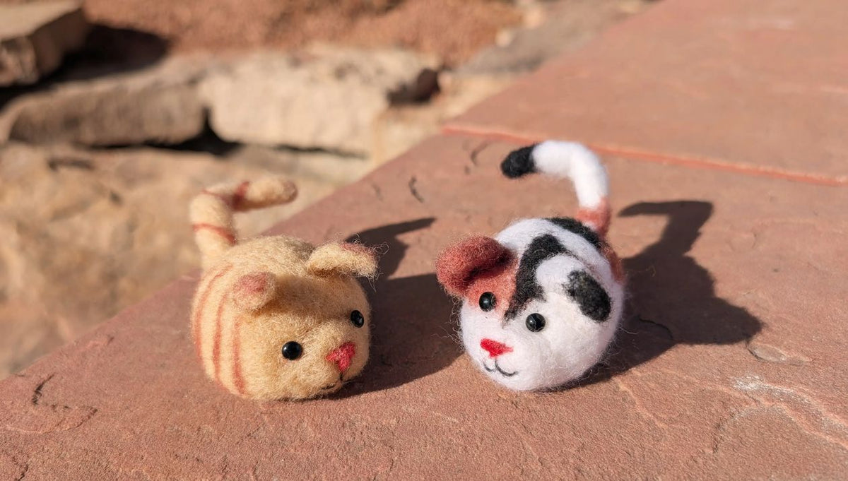 Two small plush toys resembling cats on a textured surface