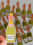 Patch of a champagne bottle with a pink bow held over multiple similar patches on a white background.