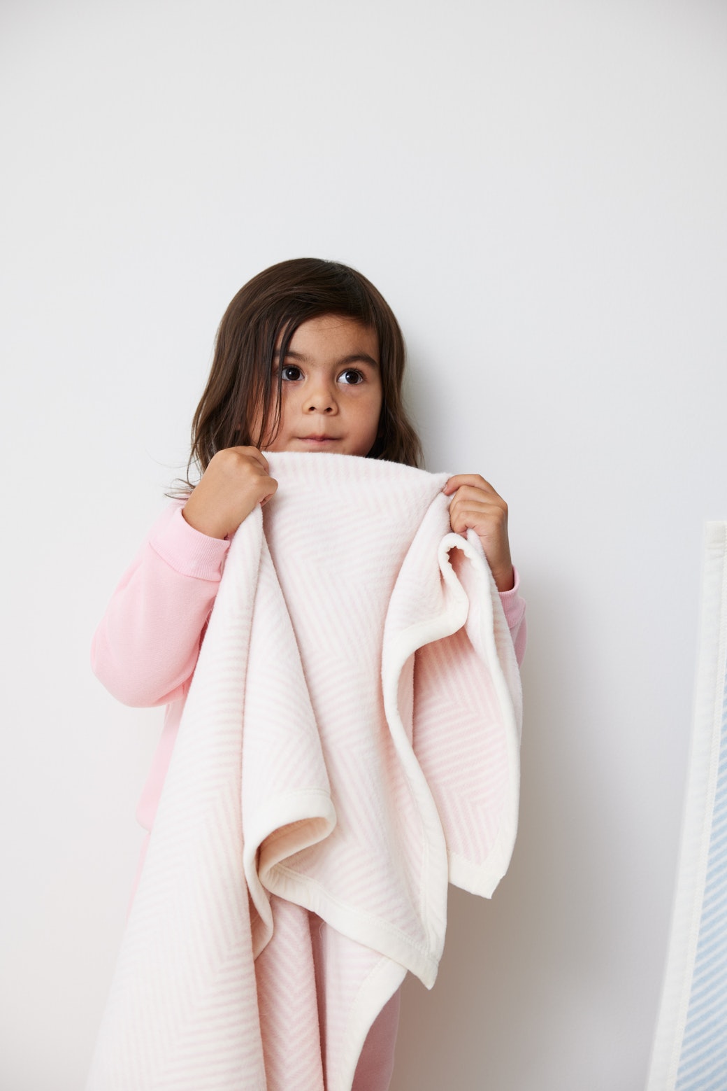 Girl wrapped in the Chappywrap Harborview Herringbone Mini Blanket in Ballet Pink