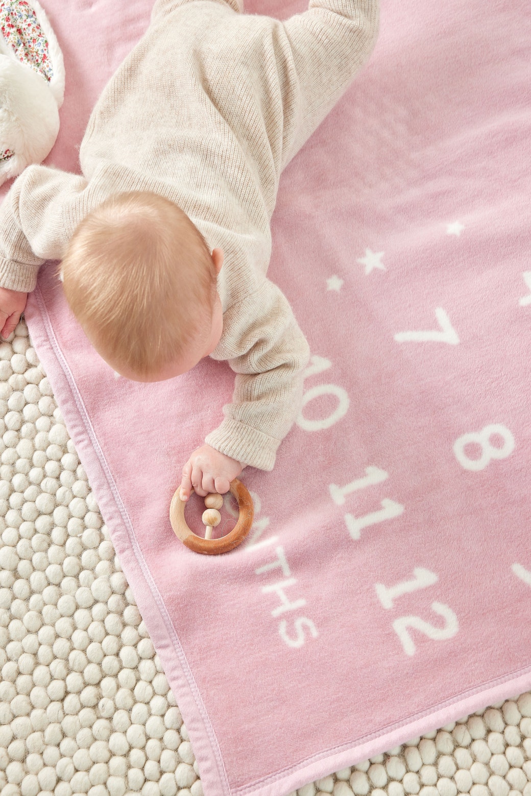 Baby lying on the Chappywrap Milestone Mini Blanket in Blush pink with month numbers 1 to 12