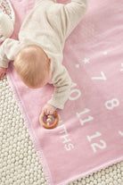 Baby lying on the Chappywrap Milestone Mini Blanket in Blush pink with month numbers 1 to 12