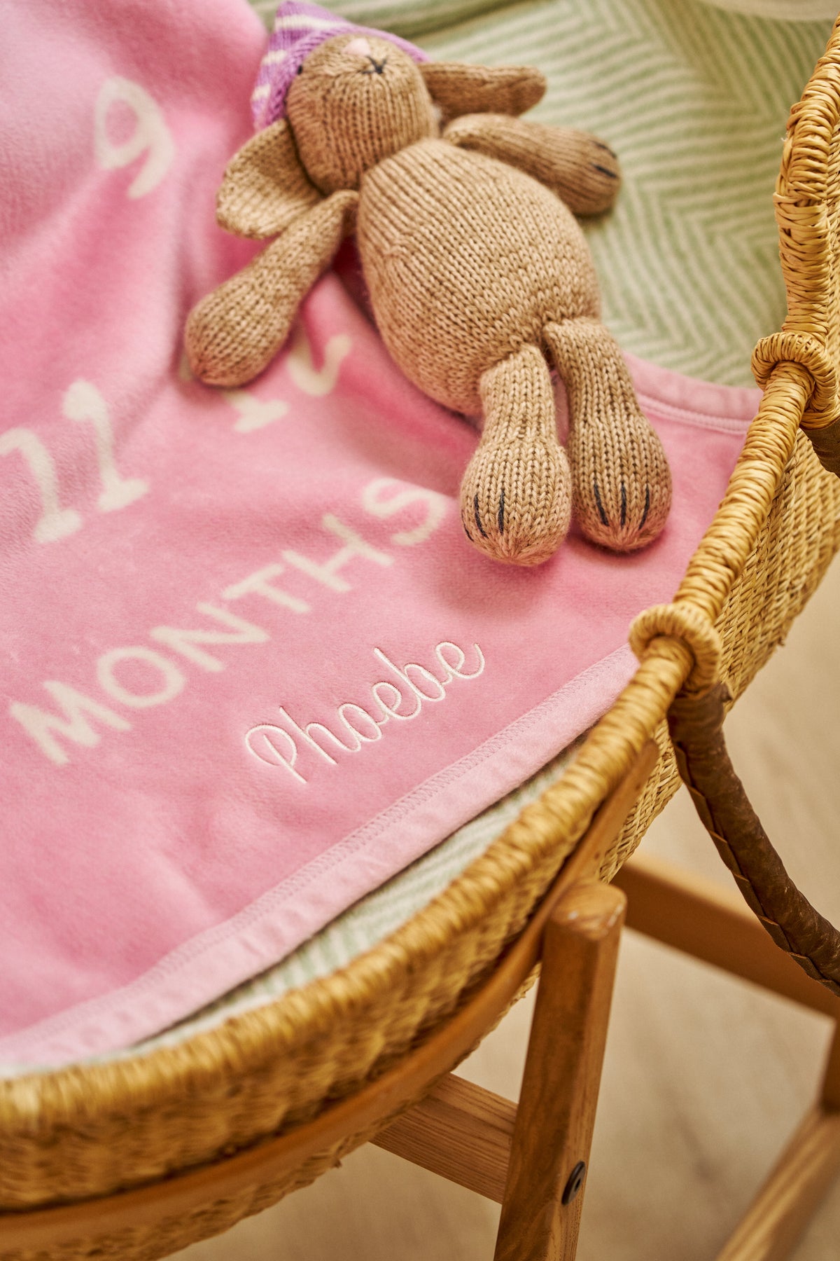 Chappywrap Milestone Mini Blanket in Blush draped in a wicker basket with a teddy bear