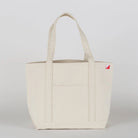 Beige tote bag with a small red logo on a light gray background