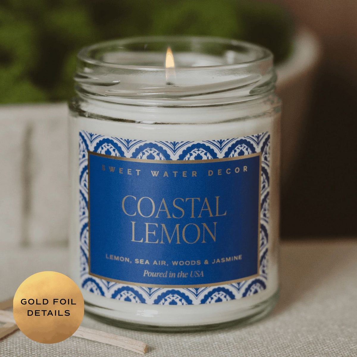 Candle in a glass jar with a blue label reading 'Coastal Lemon' from Sweet Water Decor, on a neutral background.