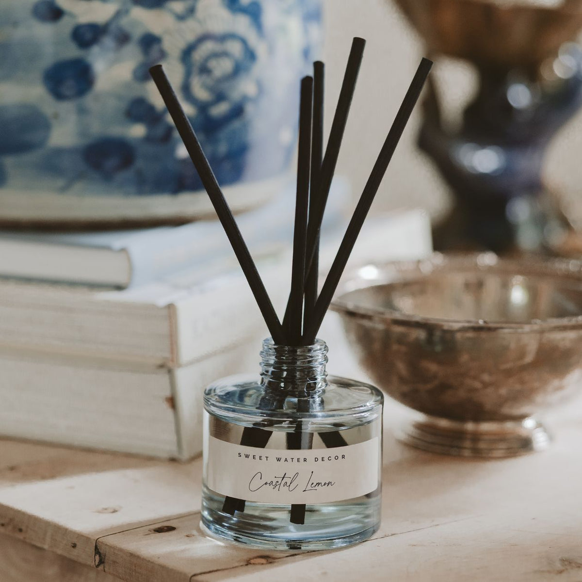 Reed diffuser with black sticks in a clear bottle on a wooden surface with decorative items in the background.