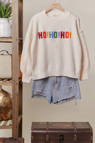 Front of the oversized ivory Colorful Christmas Sweater with multicolor HO HO HO lettering on the chest, styled with denim shorts