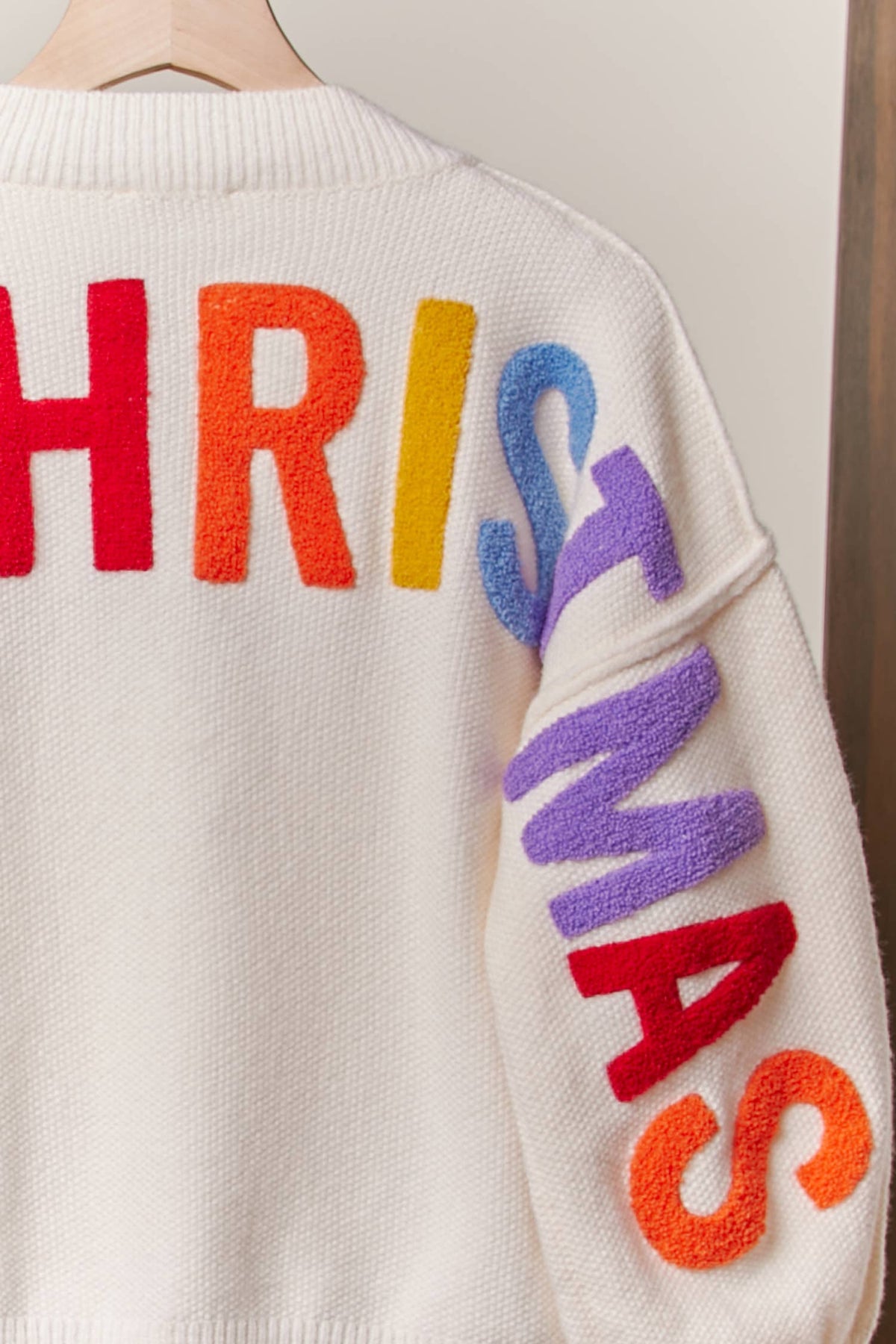 Close-up of the rainbow Christmas lettering down the sleeve of the ivory sweater