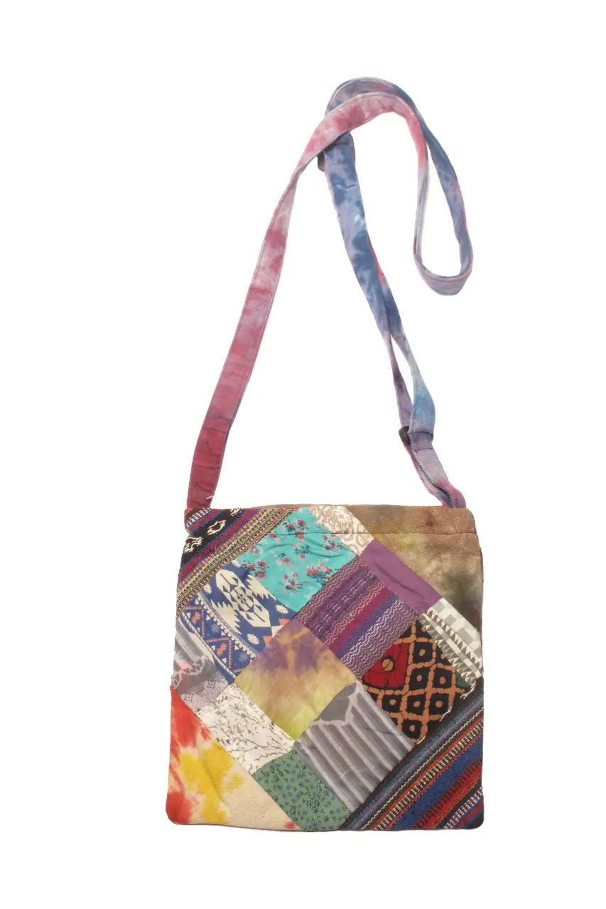A small crossbody bag with a colorful patchwork print featuring various geometric and floral textile patterns, complete with a tie-dye strap in pink, blue, and purple, shown against a plain white background.