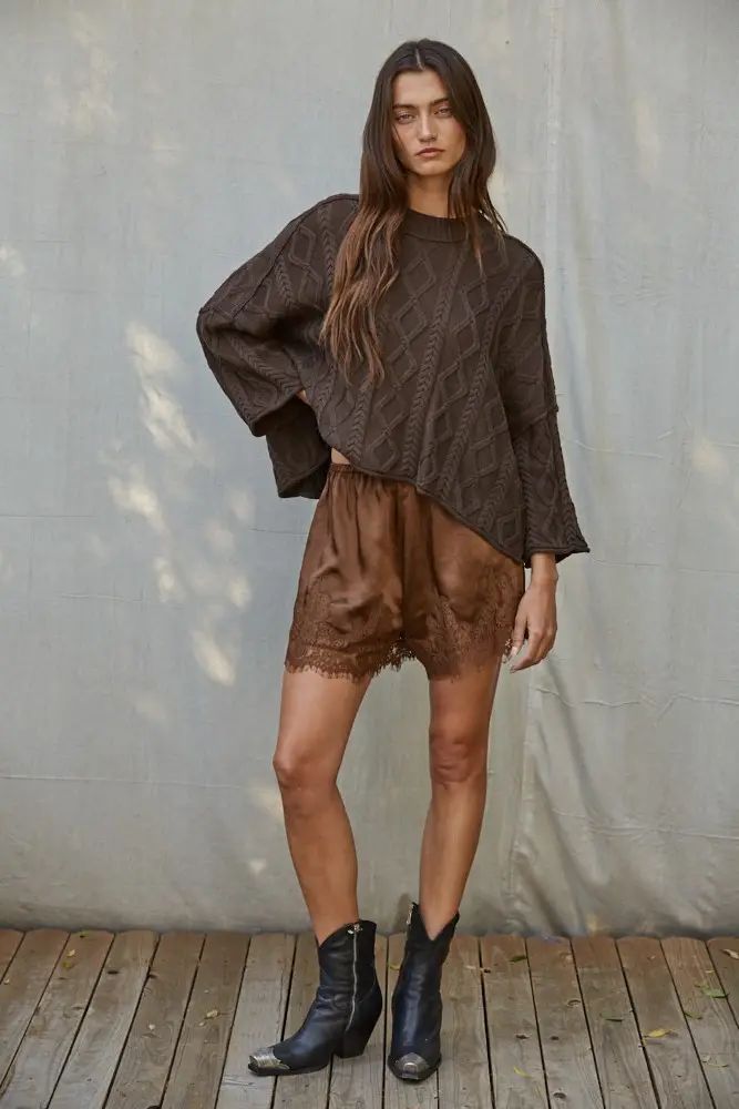 Dark brown oversized cable-knit cotton pullover sweater with three-quarter sleeves, styled with a brown lace-trim slip skirt and black boots