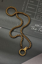 Gold chain necklace on a gray surface with a branded paper underneath