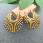 Gold-plated fan-shaped hoop earrings with inlaid CZ stones on a gray surface with green leaves in the background