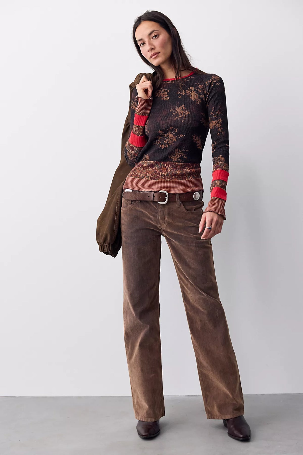 Model wearing the Free People Easy Does It Printed Top, a fitted black long sleeve tee with rust floral print and red striped cuffs and hem, with brown corduroy pants