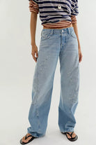 Model wearing the Free People Fable Twisted Seam Jean in Art School, low-rise light wash barrel-leg jeans with paint-fleck details, styled with a striped top and flip-flops