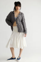 Model wearing the Free People Opal Cable Knit Cardigan in Steel Grey with a white skirt, full-length front view