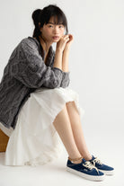 Model seated in the Opal chunky cable knit cardigan in Steel Grey, oversized with dropped shoulders