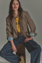 Model seated in the Shiloh plaid blazer in brown with a yellow top and wide-leg jeans