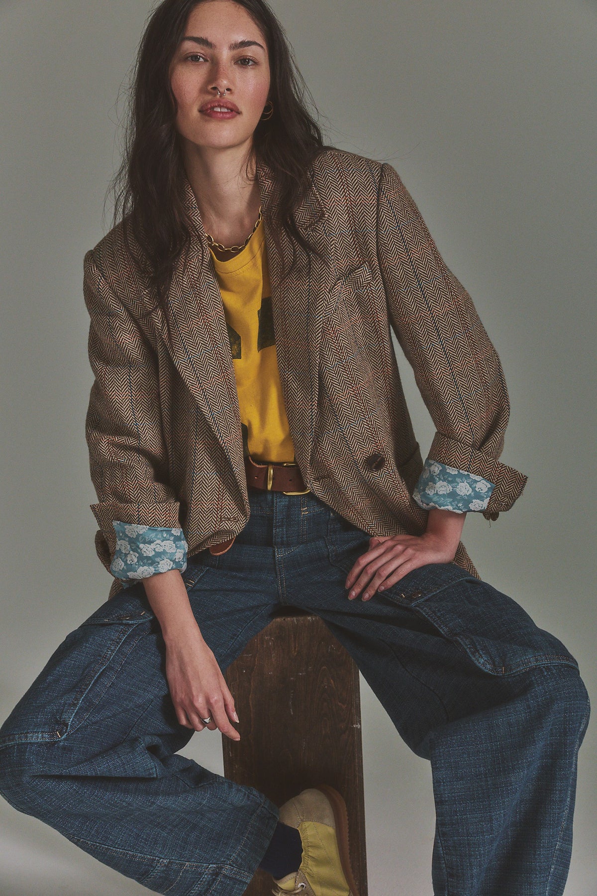 Model seated in the Shiloh plaid blazer in brown with a yellow top and wide-leg jeans