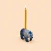 A small blue bear-shaped pencil holder with a single yellow pencil inserted, shown against a solid pale peach background.