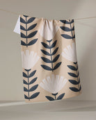 Geometry Gloria tea towel laid flat with black leaf stems on a sand background