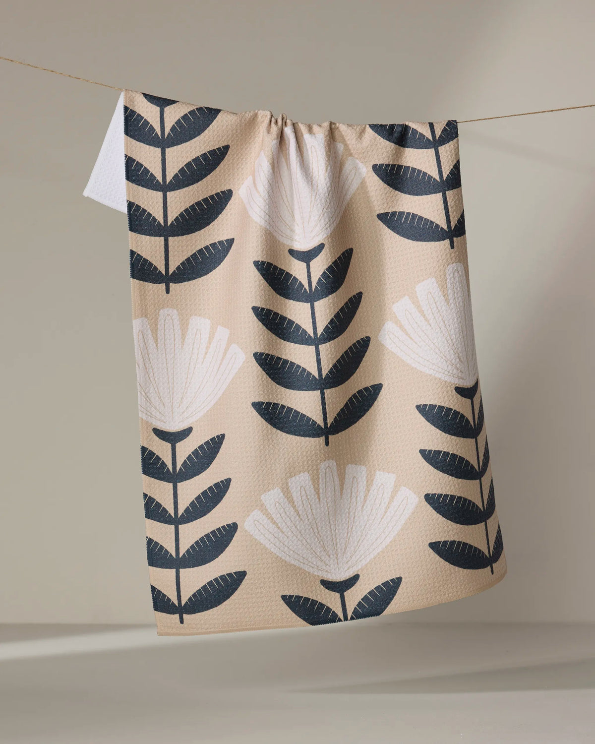 Geometry Gloria tea towel laid flat with black leaf stems on a sand background