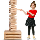 Child playing with a large wooden block tower game on a white background