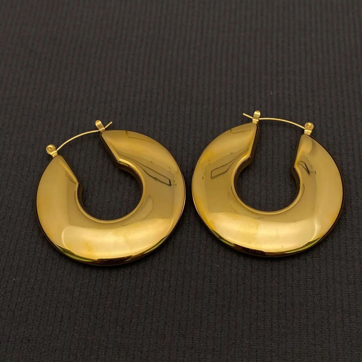 Pair of glossy gold-plated chunky hoop earrings on a black textured background