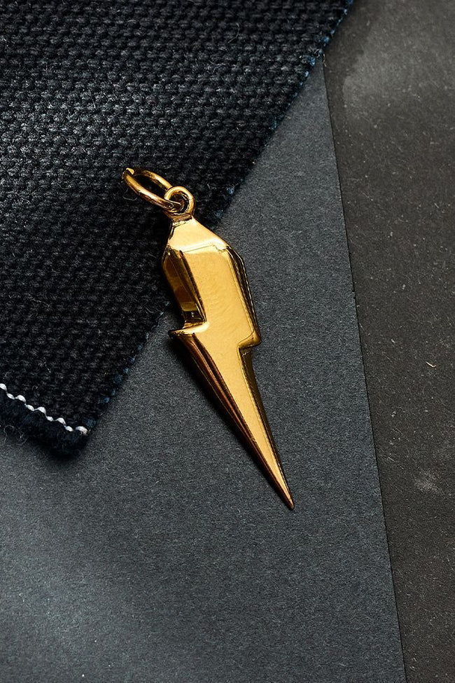 Gold lightning bolt pendant on a textured black surface