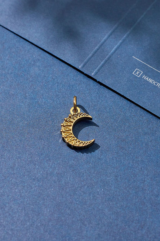 Gold crescent moon pendant on a blue surface