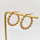 Pair of gold-plated stainless steel beaded hoop earrings on a display stand