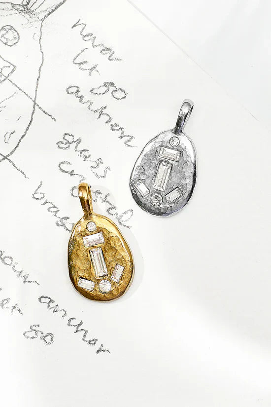 Two pendants, one gold and one silver, on a piece of paper with text.