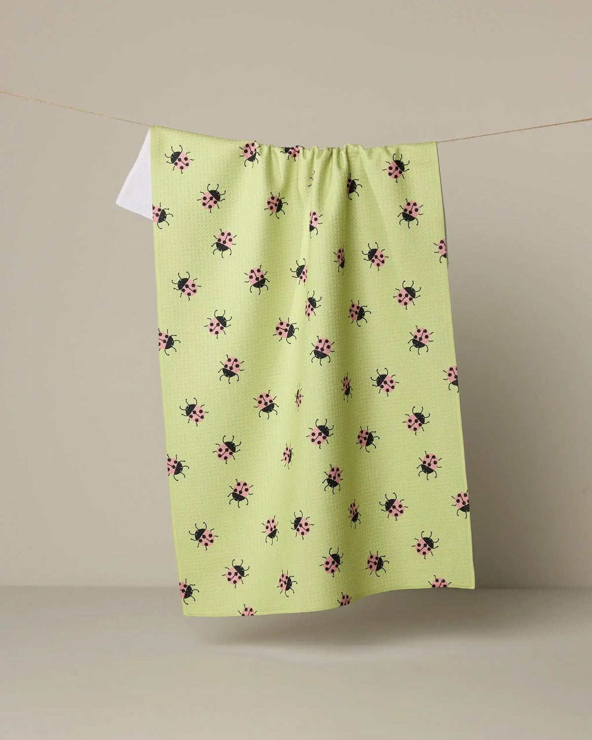 Green dishtowel with black and pink floral pattern hanging on a line against a beige background