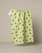 Green dishtowel with black and pink floral pattern hanging on a line against a beige background