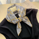 Gray floral scarf with yellow details tied around a black garment on a light background