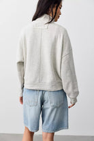 A woman shown from the back wearing a light heather gray oversized sweatshirt and light blue denim shorts against a plain light gray studio background.