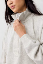 Close-up of a person wearing a light heather gray quarter-zip sweatshirt, pulling the zipper tab with one hand.