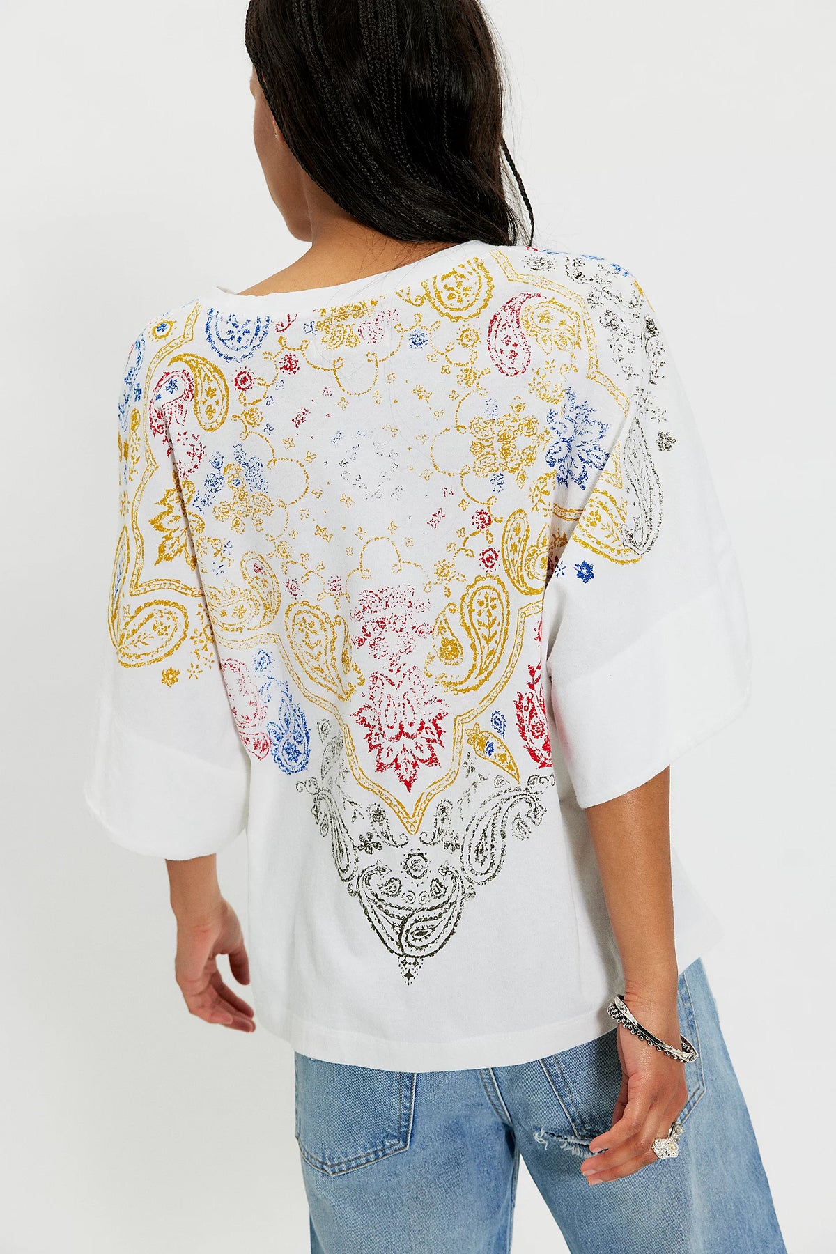 White blouse with colorful paisley pattern worn by a person on a white background