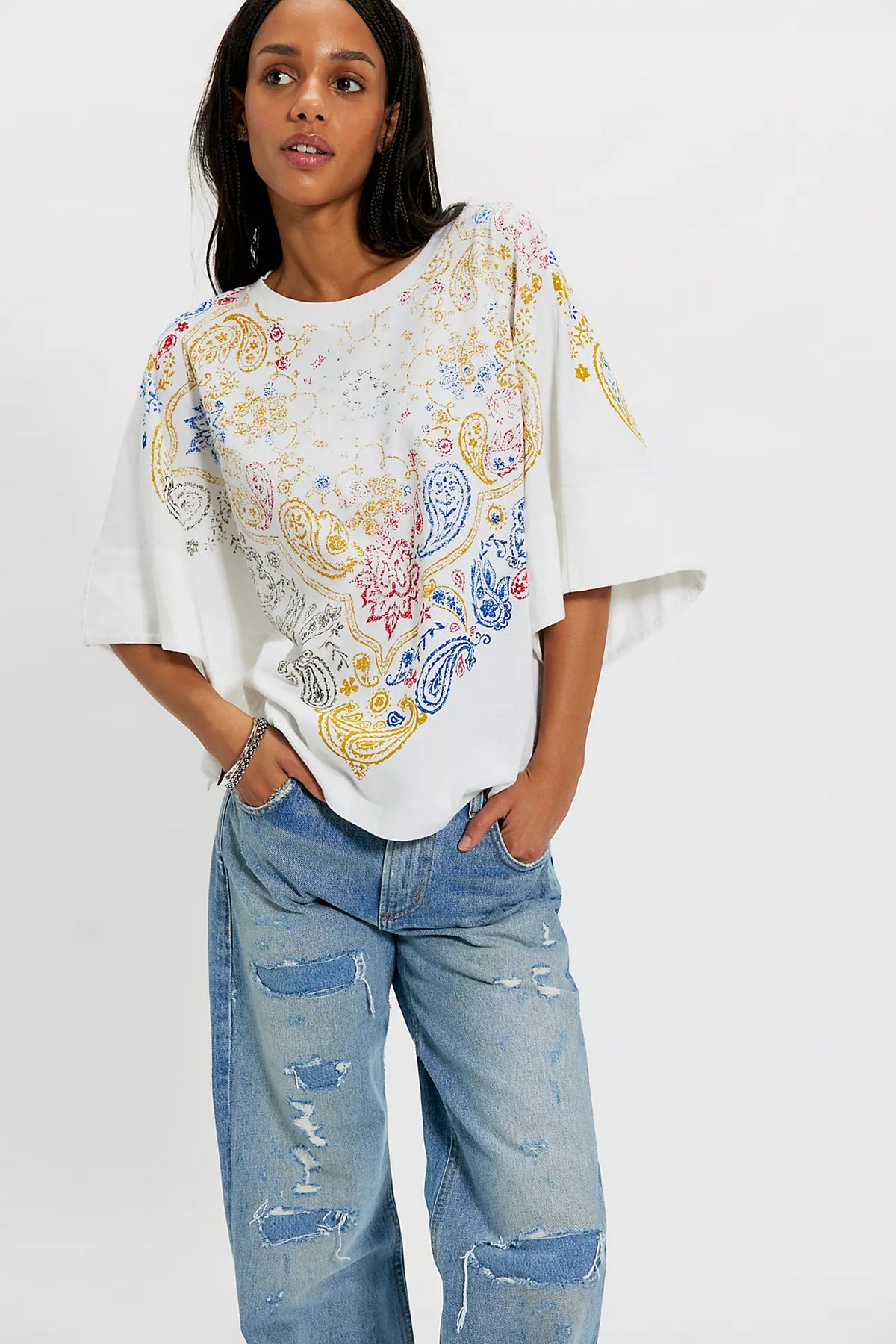 Woman wearing a colorful paisley top and blue jeans on a white background