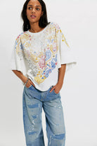 Woman wearing a colorful paisley top and blue jeans on a white background