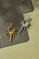 Two metallic pendants, one gold and one silver, on a textured green surface.