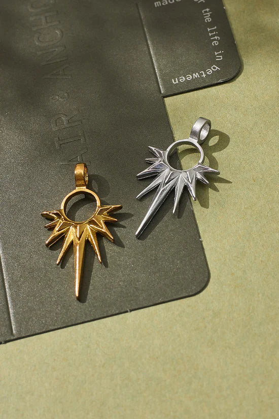 Two metallic pendants, one gold and one silver, on a textured green surface.