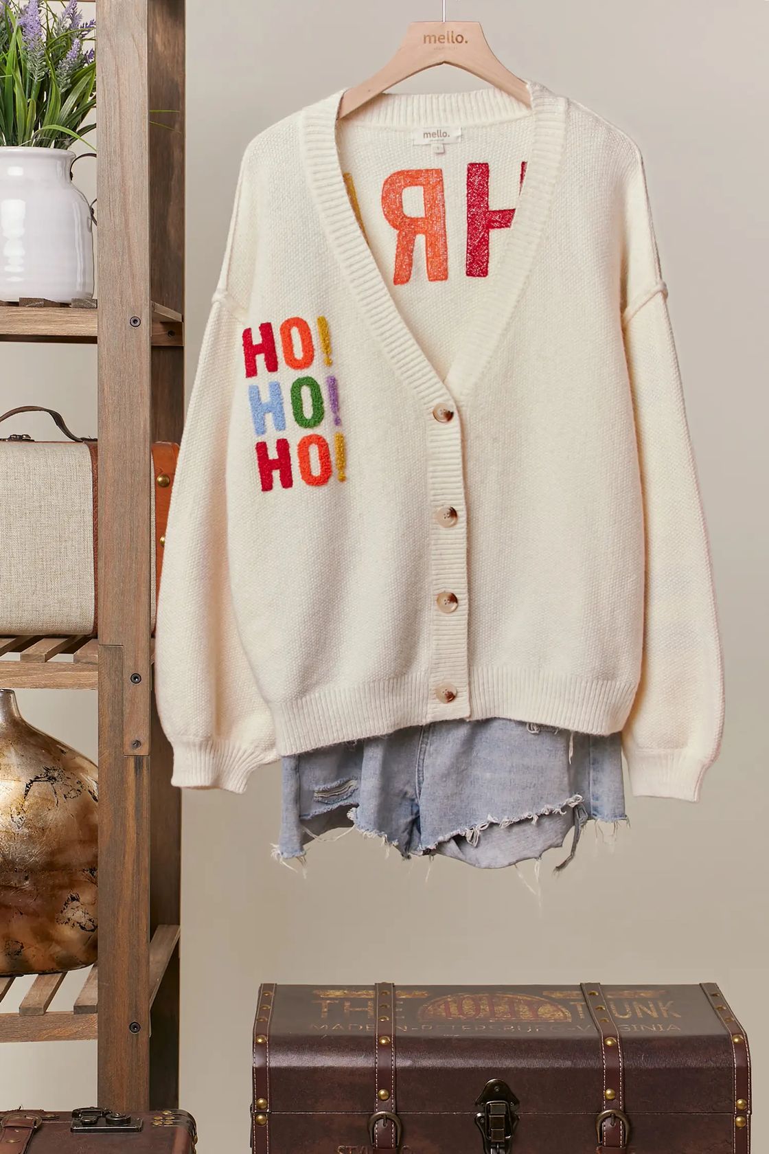 Ivory V-neck button-front cardigan with multicolor sparkly HO HO HO lettering on the chest, styled with denim shorts on a wooden hanger