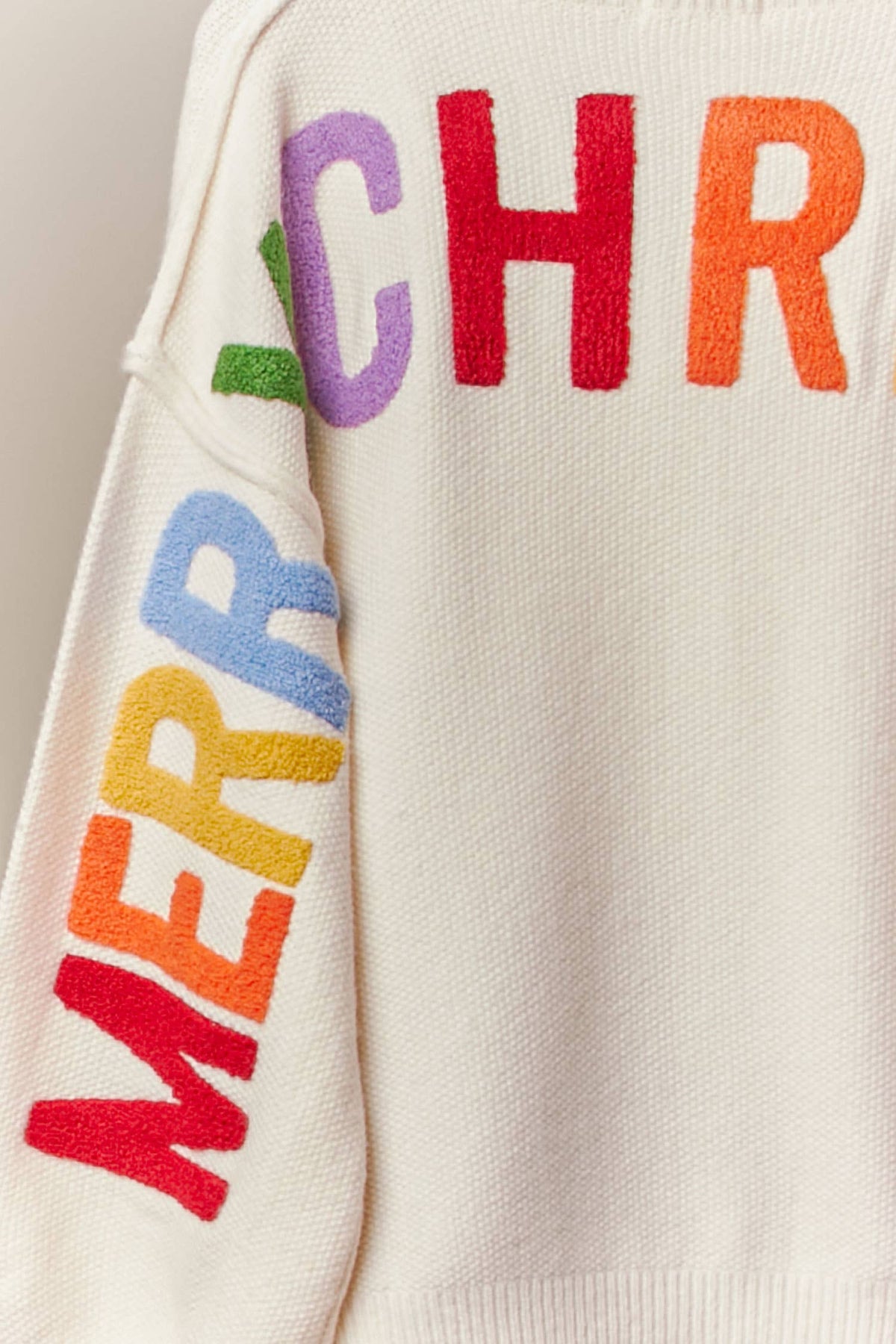 Close-up of the rainbow Merry Christmas letters on the back of the ivory cardigan