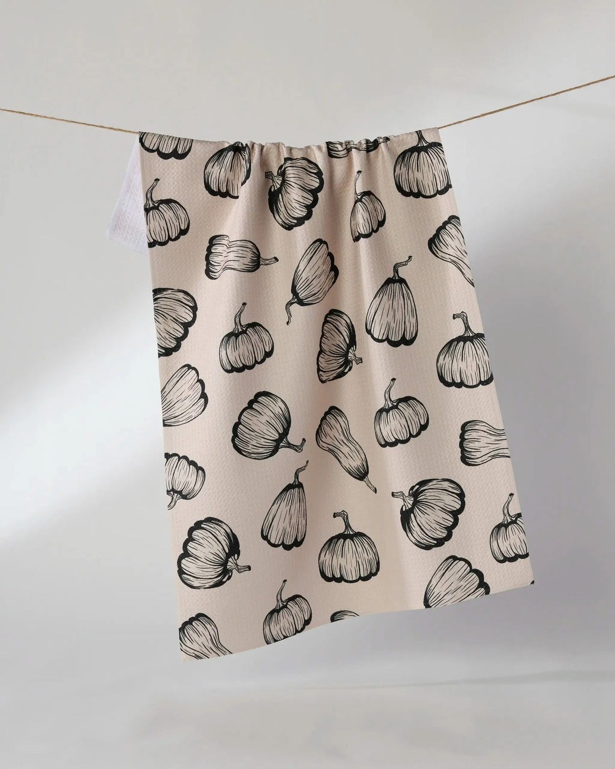 Hollow Season Halloween tea towel in soft blush with black pumpkin print hanging on a line