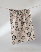 Hollow Season Halloween tea towel in soft blush with black pumpkin print hanging on a line