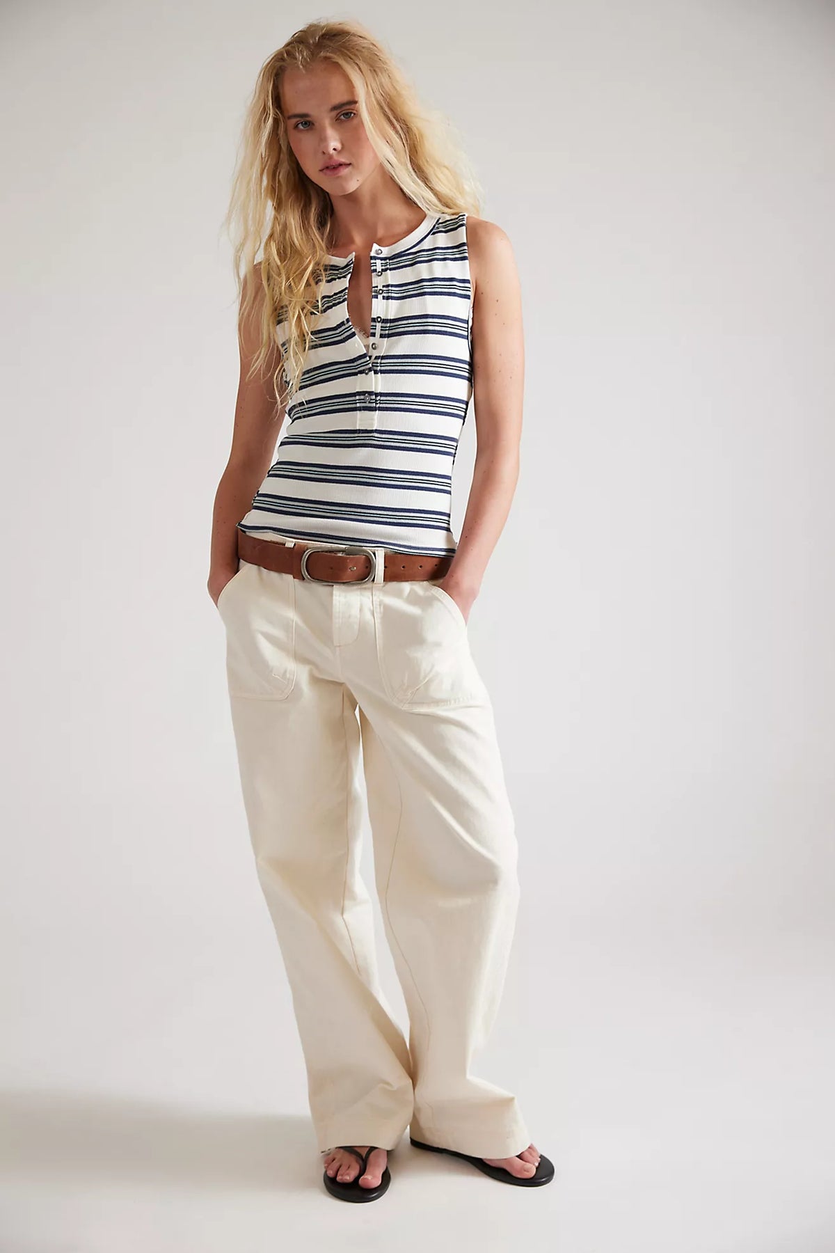 Woman wearing a striped sleeveless top and white pants on a plain background