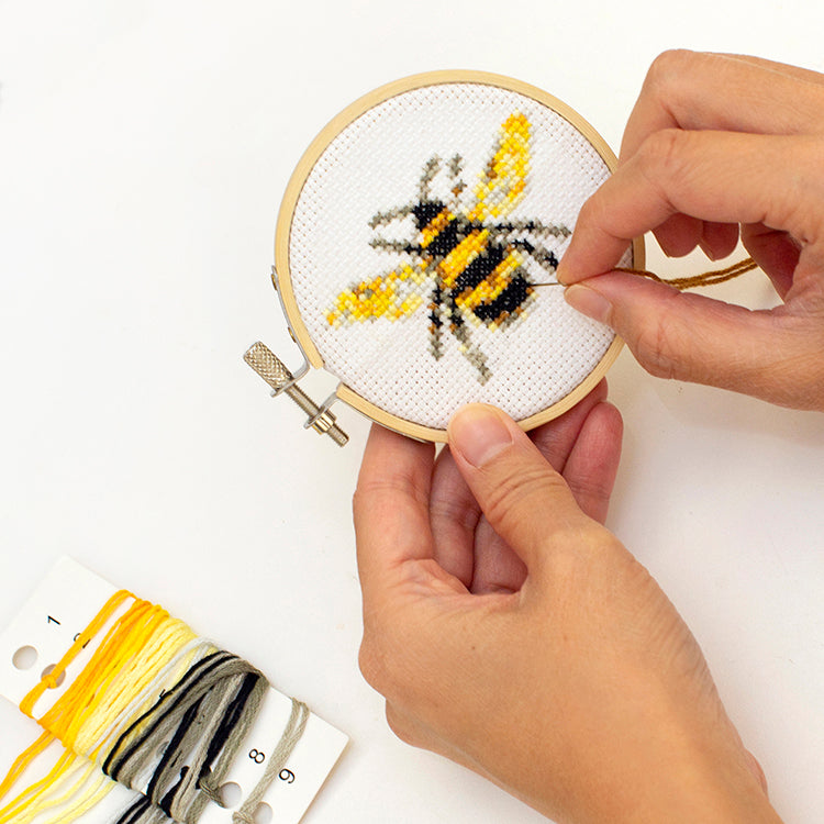 Hands stitching the Kikkerland bee mini cross stitch in a hoop