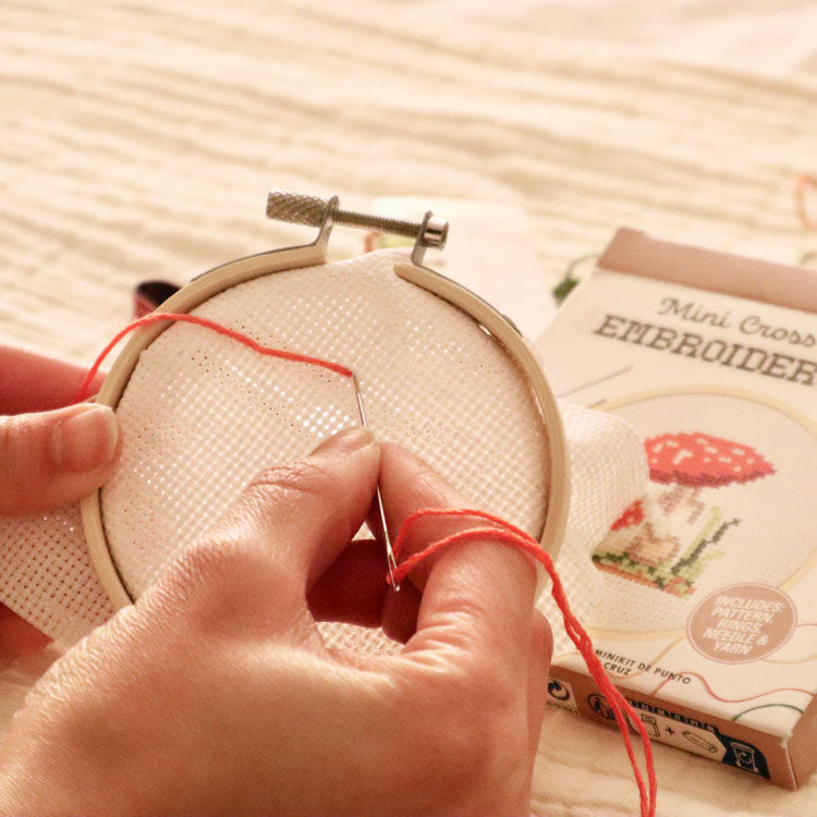 Hands stitching the Kikkerland mushroom mini cross stitch embroidery kit