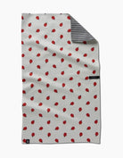 A white waffle-weave kitchen towel with a red ladybug pattern, featuring a striped black and white reverse side and small black brand labels.