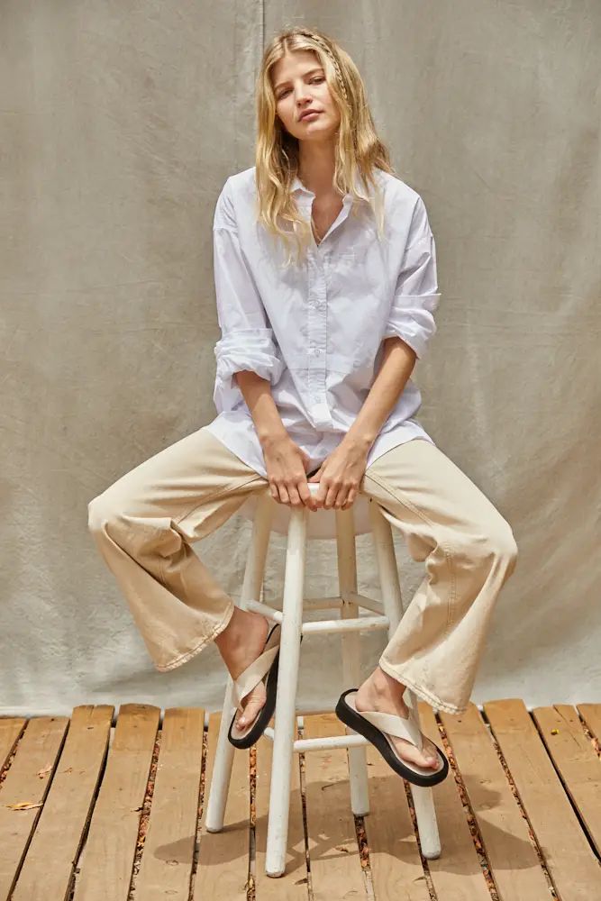 Light blue oversized woven cotton button-down shirt with a pointed collar and rolled long sleeves, styled with beige wide-leg pants